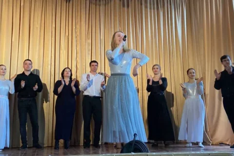 Солістка в блакитній сукні співає на сцені серед музикантів на концерті