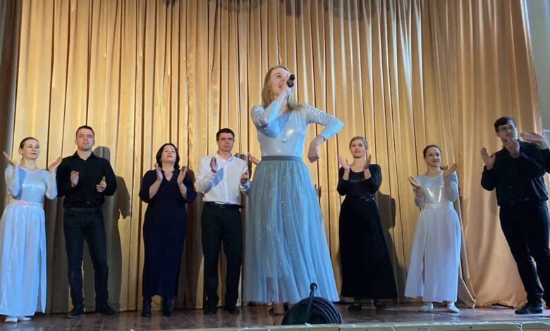 Солістка в блакитній сукні співає на сцені серед музикантів на концерті
