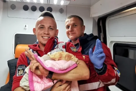 Двоє медиків швидкої в салоні карети тримають немовля в рожевій ковдрі